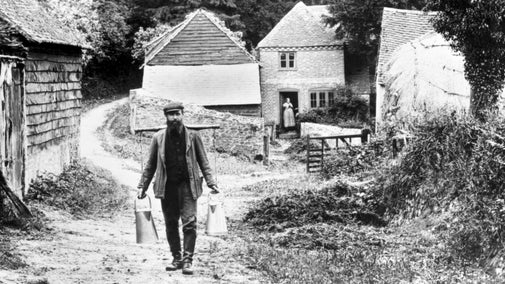 Black and white image of bearded George Mayes standing in front of the broom squires cottages in1907